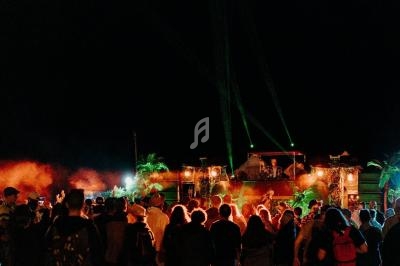 Foule rassemblée devant une scène illuminée avec des effets de lumière et de la fumée, en extérieur de nuit.