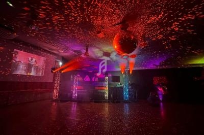 Salle sombre avec éclairages colorés, projecteurs, boule disco et ambiance festive.