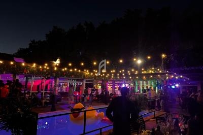 Terrasse animée en soirée avec guirlandes lumineuses, piscine, et personnes profitant d'une ambiance festive.