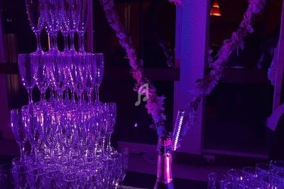 Tour de coupes de champagne éclairée en violet avec une bouteille et un cœur décoratif en arrière-plan.