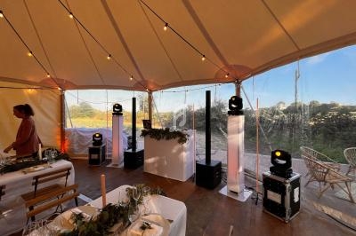 Intérieur d'une tente décorée pour un événement, avec tables dressées, guirlandes lumineuses et matériel de sonorisation.