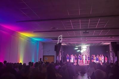 Des personnes sur scène sous des éclairages colorés, devant un public assis dans une salle sombre.