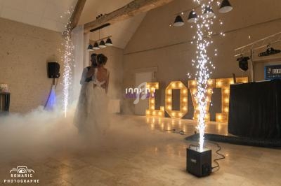 Un couple danse dans une salle décorée avec des lettres lumineuses ’LOVE’ et des effets pyrotechniques.