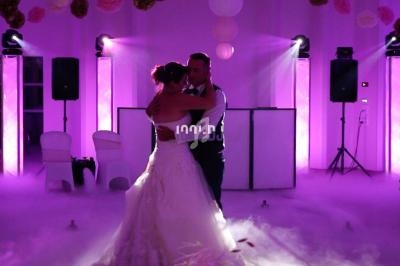 Un couple danse dans une salle éclairée de lumières violettes, entourée de fumée au sol.