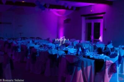 Salle de réception décorée avec des nappes blanches et éclairée par une lumière violette tamisée.