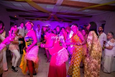 Des personnes dansent dans une salle décorée avec des guirlandes, sous un éclairage coloré.