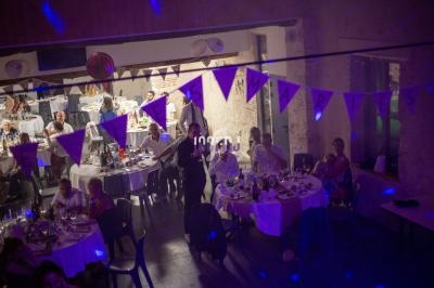 Salle de réception décorée avec des guirlandes, des invités assis autour de tables dressées pour un événement festif.