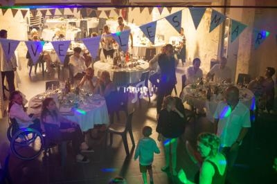 Des invités assis et debout dans une salle décorée pour une fête, avec une guirlande ’Vive les mariés’.