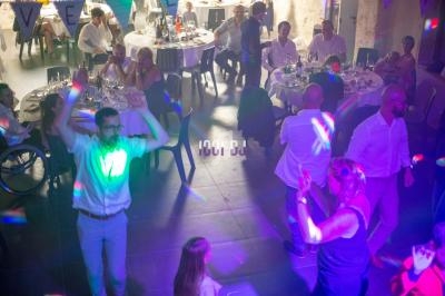 Des personnes dansent et dînent dans une salle éclairée par des lumières colorées lors d'un événement festif.