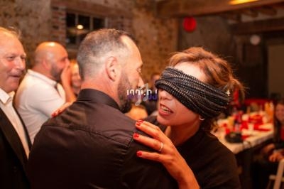 Une femme aux yeux bandés touche un homme dans une ambiance festive avec des invités en arrière-plan.