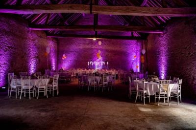 Salle de réception en pierre avec tables dressées, éclairage violet et ballons décoratifs.