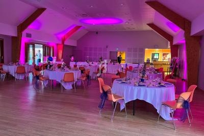 Salle de réception décorée avec des tables rondes dressées, éclairage rose et ambiance festive.