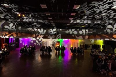 Salle de réception avec éclairages colorés et motifs lumineux au plafond, des groupes de personnes assises à des tables.
