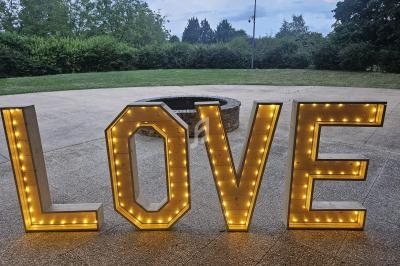 Lettres lumineuses formant le mot ’LOVE’ posées sur une terrasse en extérieur, avec un jardin en arrière-plan.