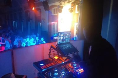 Un DJ mixe sur une console éclairée, face à une piste de danse animée dans une salle aux lumières colorées.