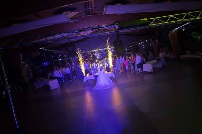 Une mariée danse au centre d'une salle éclairée, entourée d'invités, avec des étincelles en arrière-plan.