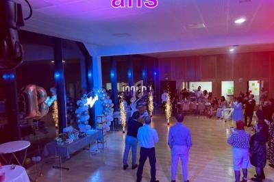 Personnes rassemblées dans une salle décorée avec des ballons et des lumières pour une fête d'anniversaire.