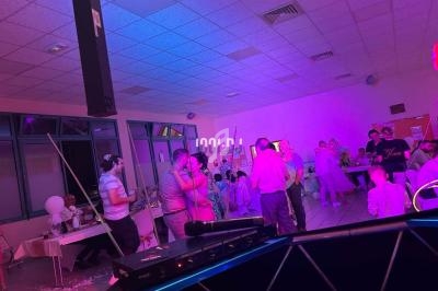 Des personnes dansent et discutent dans une salle éclairée par des lumières colorées lors d'un événement festif.