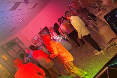 Des invités dansent et discutent dans une salle éclairée par des lumières colorées lors d'une fête ou d'un événement.