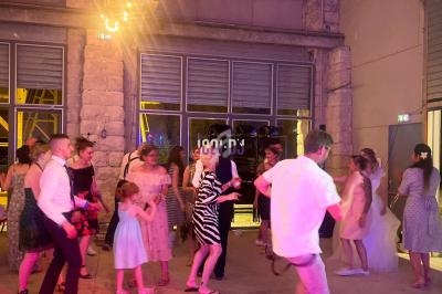 Des personnes dansent dans une salle éclairée par des guirlandes lumineuses, avec un sol en béton et des murs en pierre.