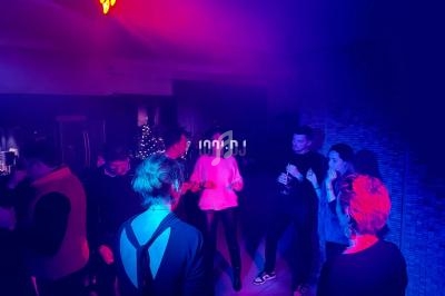 Des personnes dansent et discutent dans une ambiance tamisée avec éclairage coloré dans une salle festive.