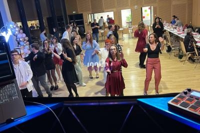 Des personnes dansent dans une salle éclairée, entourées de tables dressées et de décorations festives.