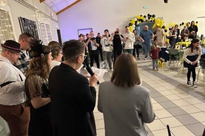 Groupe de personnes rassemblées dans une salle décorée de ballons noirs et jaunes, lors d'un événement festif.