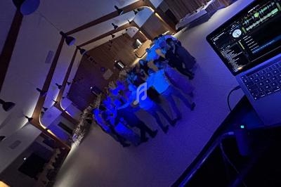 Groupe de personnes dansant en cercle dans une salle éclairée par des lumières bleues, avec un ordinateur de DJ au premier…