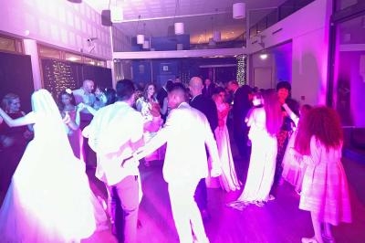 Des invités dansent dans une salle éclairée de lumières colorées, lors d'une fête ou d'une célébration.