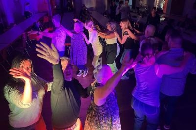 Des personnes dansent en groupe dans une salle éclairée par des lumières colorées, créant une ambiance festive.