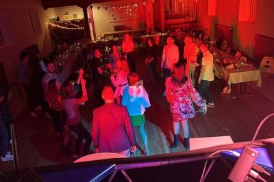 Des personnes dansent dans une salle éclairée par des lumières rouges, entourées de tables dressées pour un événement.