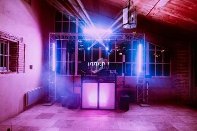 Installation de DJ avec éclairage coloré et fumée dans une salle au plafond en bois et murs en briques.