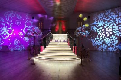 Escalier illuminé menant à une porte, entouré de décorations florales et de projections lumineuses sur les murs.
