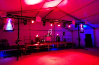 Scène éclairée de lumières rouges et violettes dans une tente, avec équipement audio et décorations suspendues.