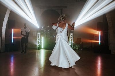 Une femme en robe de mariée danse dans une salle éclairée par des projecteurs colorés.