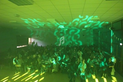 Salle remplie de personnes assises à des tables, éclairée par des lumières vertes et des motifs projetés au plafond.