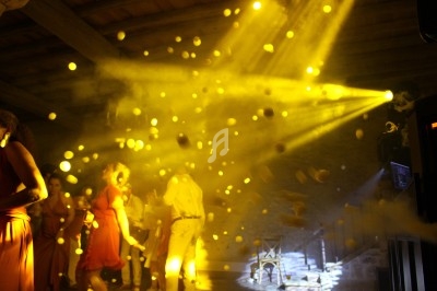 Des personnes dansent sous des lumières jaunes vives dans une salle avec un plafond en bois.