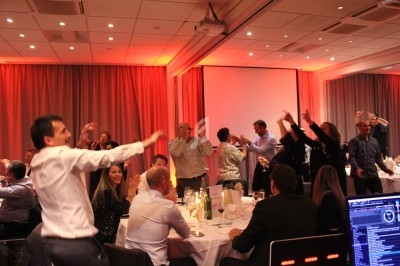 Des personnes dansent et s'amusent lors d'un dîner festif dans une salle éclairée par des lumières chaudes.