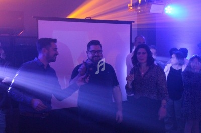 Des personnes discutent et sourient dans une ambiance festive avec des lumières colorées et un écran en arrière-plan.