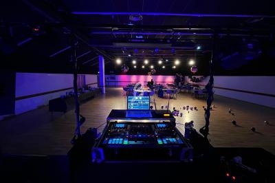 Vue depuis une régie DJ éclairée sur une salle sombre avec des tables, des chaises et des ballons au sol.