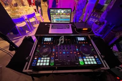 Table de mixage DJ avec un ordinateur portable affichant un logiciel de musique, entourée d'invités lors d'un événement.