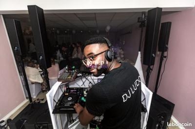 Un DJ mixant sur une table de mixage dans une salle éclairée, entouré d'équipements audio.