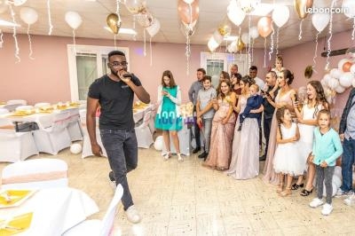 Un homme chante au micro devant un groupe de personnes rassemblées dans une salle décorée pour une fête.