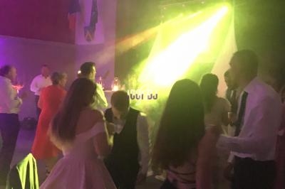 Des personnes dansent dans une salle éclairée par des lumières colorées, avec un DJ en arrière-plan.