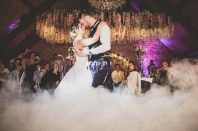 Un couple danse sous un éclairage coloré et une décoration florale, entouré de fumée et d'invités.