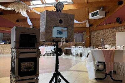 Borne photo installée dans une salle de réception décorée, avec tables dressées et lumière naturelle.