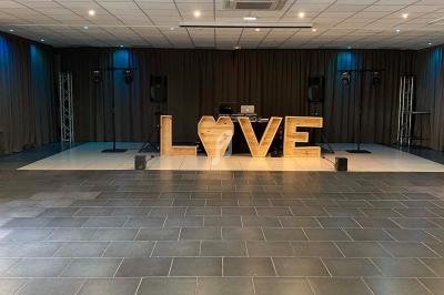 Salle de réception avec une décoration lumineuse en bois formant le mot ’LOVE’ devant une scène équipée de matériel audio.