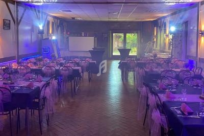 Salle de réception décorée avec des tables dressées, des chaises ornées de nœuds roses et un éclairage tamisé.