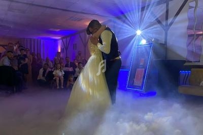 Un couple danse dans une salle éclairée, entouré de fumée au sol et d'invités assis en arrière-plan.