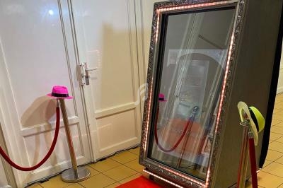 Miroir interactif encadré, entouré de lumières LED, placé sur un tapis rouge avec des chapeaux colorés à proximité.
